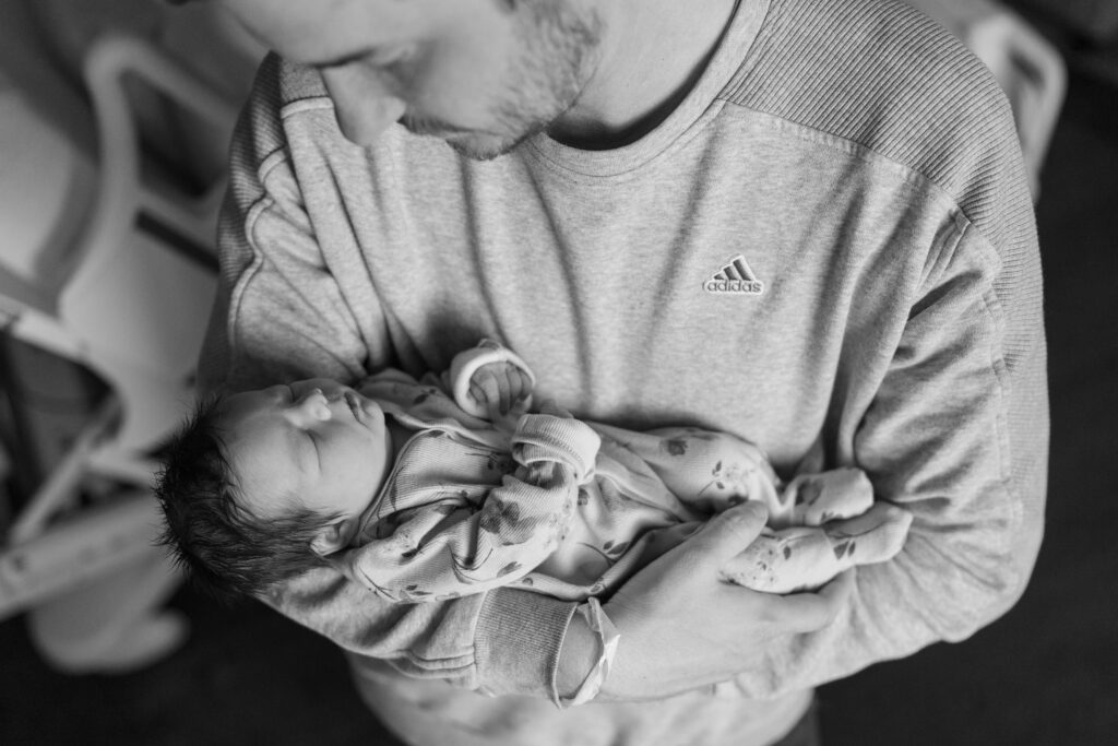 black and white photo of dad cradling newborn baby girl in his arms during fresh 48 photos and film session at hospital