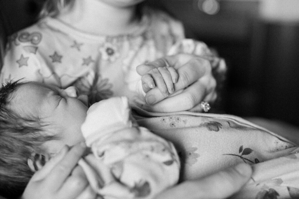 black and white photo of big sister looking at newborn baby's fingers at hospital during fresh 48 photos and film session