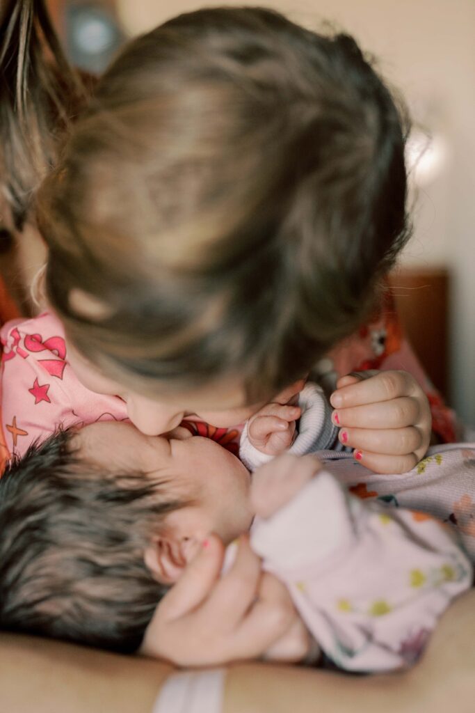 a closeup of big sister giving newborn baby a kiss on the nose