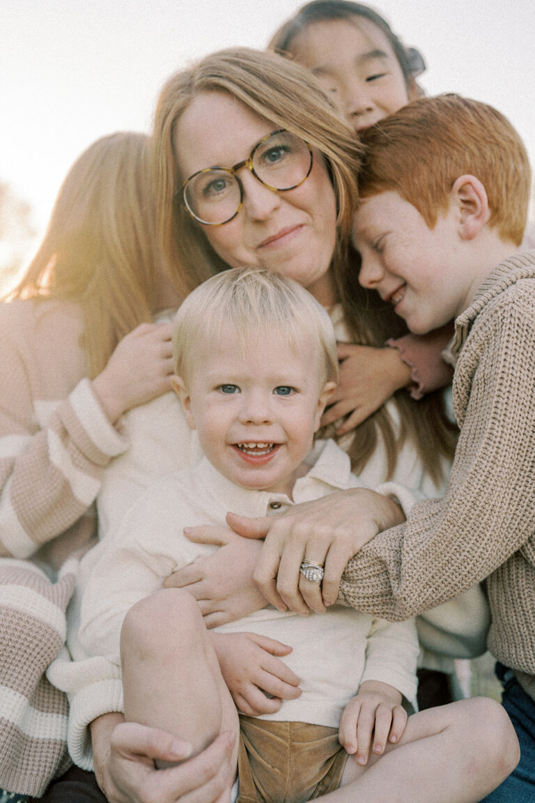 photograph of mother with her arms intertwined with her four children softly smiling at the camera